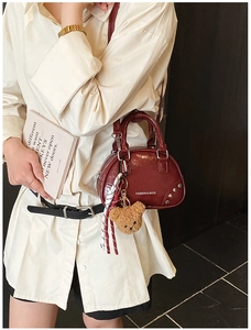 Detail of wine red glossy handbag with metal studs and cute plush bear charm accessory