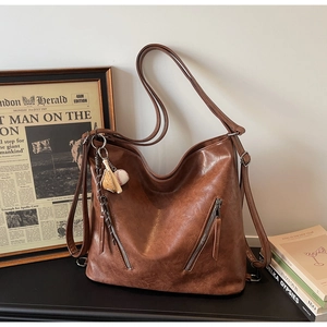 Detailansicht einer braunen Vintage-Leder-Tote mit zwei Reißverschlüssen und Baseball-Anhänger