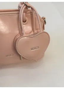 Detail of light pink shell bag featuring a heart-shaped charm with silver MUHETI logo