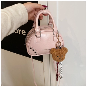 Detail of pink mini boston bag featuring metallic studs and brown plush bear charm