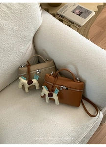 Détail de deux sacs en cuir grainé avec breloques de cheval sur un canapé moelleux