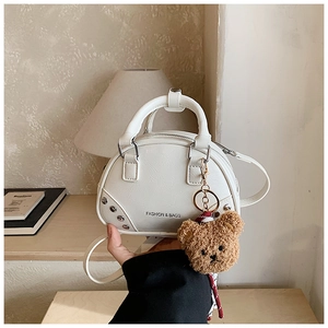 Detail of white bowling bag with textured leather, teddy bear charm and metal rivets