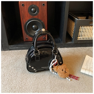 Detail of black semi-circular handbag with silver rivets and cute bear charm pendant