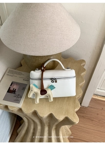Détail d'un sac à main blanc en cuir grainé avec un charm cheval coloré sur une table en bois