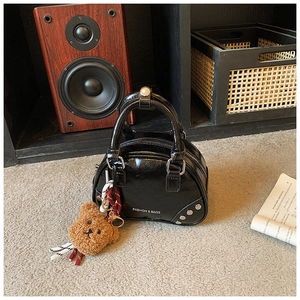 Detail of glossy black mini bowling bag with rivets and a cute brown plush bear charm