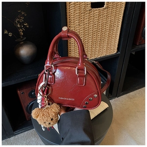 Detail of dark red patent leather bowling bag with silver studs and a plush bear charm