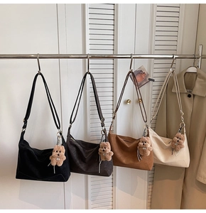 Detail showing four matte PU shoulder bags with plush bear charms on a metal display rack
