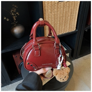Detail of burgundy leather bowling bag with silver studs and cute teddy bear charm