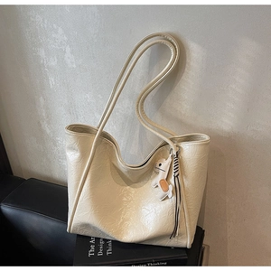 Detailed view of cream tote bag with crinkled texture, dog charm and tassel detail