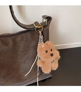Close-up of a brown plush dog charm with pearl necklace attached to a leather bag
