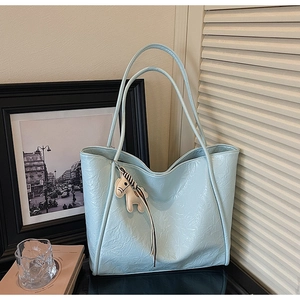 Detail of light blue tote bag with pleated texture and stylish cream horse pendant accessory