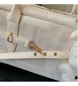 Detailed close-up of textured canvas fabric and shiny golden metal hardware on a cream handbag