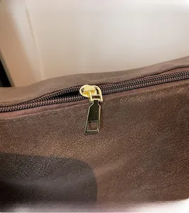 Detailed close-up of smooth gold metal zipper and leather texture on a coffee brown handbag