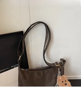 Detail of dark brown leather shoulder bag with gold hardware and plush bear charm