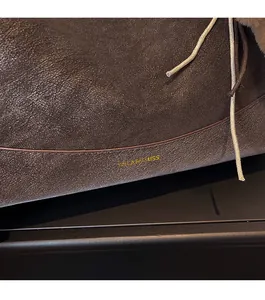 Close-up of dark brown leather handbag featuring golden logo and ivory drawstring detail