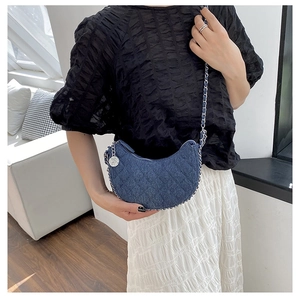 Detail of blue denim crescent bag with quilted diamond pattern and silver rose charm