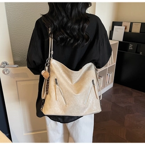 Detailansicht der cremeweißen Kunstledertasche mit Reißverschlüssen und Baseball-Anhänger