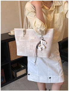 Detail of beige tote bag with geometric pattern and cute white horse charm on a model