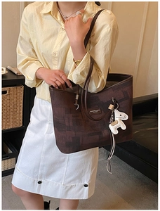 Brown leather tote bag detail with decorative white horse charm on a leather sofa