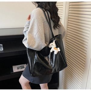 Detailed macro view of a glossy black patent leather tote bag with a white horse charm