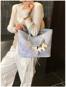 Detail of light blue geometric tote bag with white horse charm and leather strap