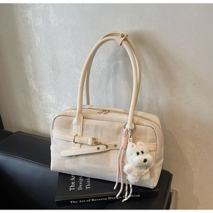 Detail of cream tote bag with gold zipper and plush dog charm on a book