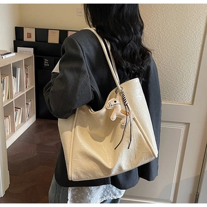 Detail of cream tote bag with wrinkled texture and horse charm shown on shoulder