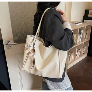 Detail of cream tote bag featuring a pony charm and fringe on smooth pleated leather