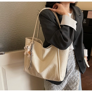 Detail of cream tote bag with pleated texture and horse charm worn over the shoulder