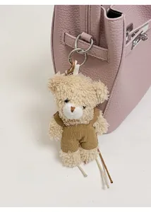 Plush brown bear charm with fashion overalls attached to a pink leather bag detail