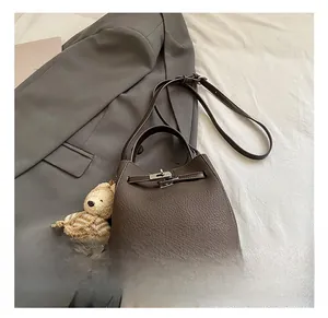 Detail of lychee pattern leather bucket bag with lock closure and bear charm accessory