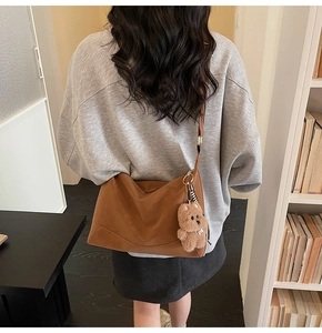 Brown frosted leather crossbody bag with a plush bear charm shown in a lifestyle scene