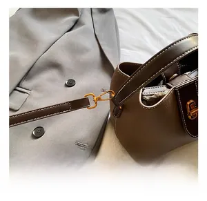 Detail of golden metal hooks and white contrast stitching on brown litchi leather bag