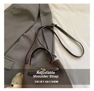Detail showing the adjustable leather shoulder strap and buckle on the brown bucket bag