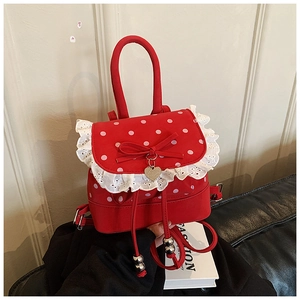 Dettaglio mini zaino rosso a pois con bordo in pizzo bianco e ciondolo a fiocco