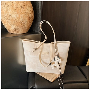 Detail of cream canvas bucket bag with grid texture, leather logo and horse charm