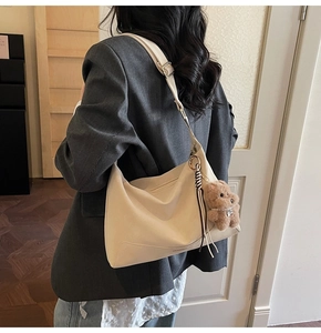 Detail of beige Hobo bag with adjustable strap and cute brown teddy bear pendant