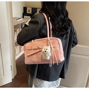 Pink fabric handbag with white plush dog pendant and tassel details in home setting