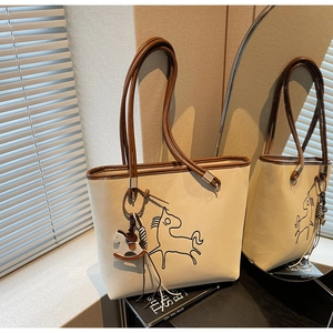 Detail of cream tote bag with horse embroidery, brown trim and matching charm accessory