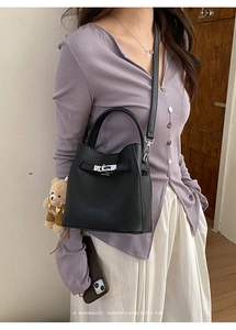 Macro detail of black litchi grain leather bucket bag with silver twist lock and bear charm