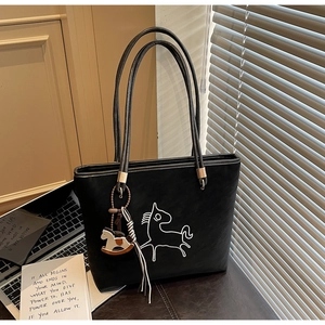 Close-up of black matte tote bag featuring minimalist horse embroidery and wooden charm
