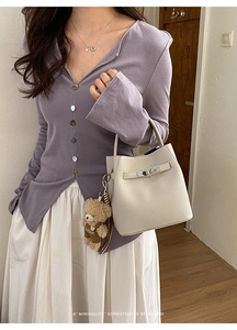 Model wearing a cream lychee leather bucket bag with a cute bear plush charm and metal clasp