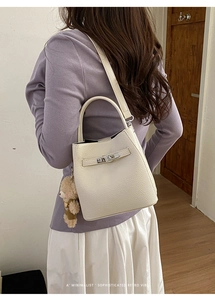 Detail view of cream bucket bag with litchi grain texture and cute bear charm