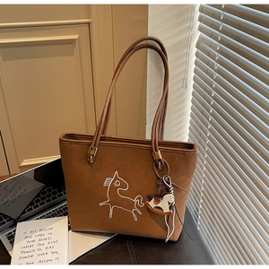 Detail of a brown suede tote bag featuring horse embroidery and a leather rocking horse charm