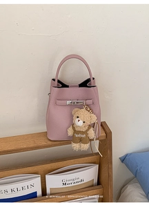 Detail of light pink pebble leather bucket bag with metal buckle and plush bear charm
