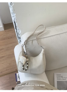 Détail du sac hobo crème avec coutures et charm en peluche posé sur un canapé blanc