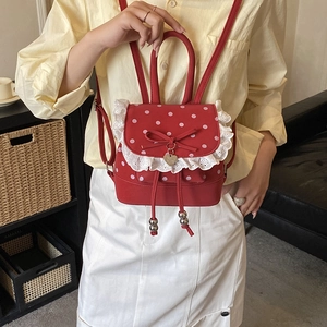 Dettaglio mini zaino rosso a pois con bordo in pizzo bianco e ciondolo a fiocco