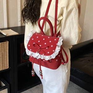 Dettaglio dello zaino rosso a pois con bordo in pizzo bianco e ciondolo a cuore in metallo