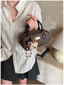 Detail of dark brown leather Boston bag with golden hardware and a cute teddy bear charm