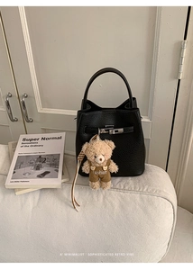Close-up of black litchi grain leather bucket bag with silver lock and teddy bear charm